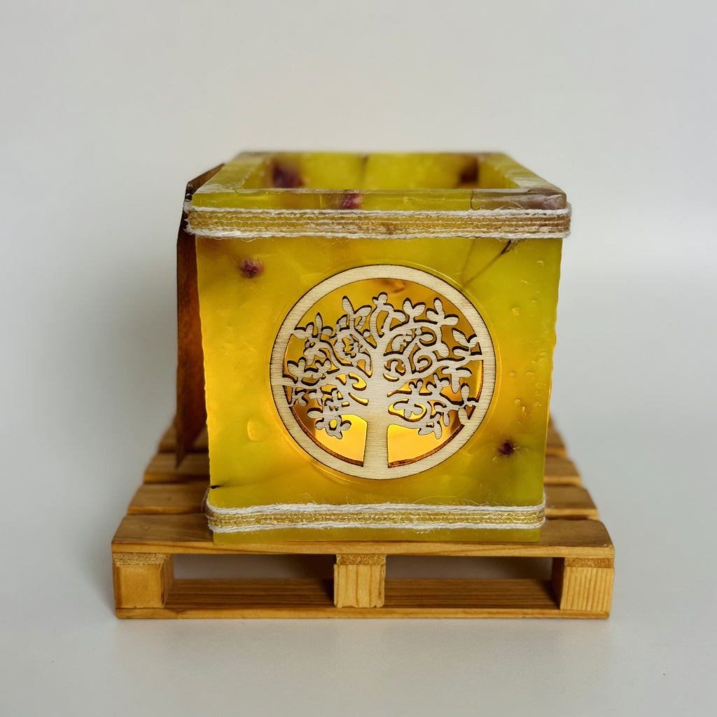 Vela hueca artesanal con símbolo del Árbol de la Vida en color amarilla, iluminada con luz LED cálida. Pieza única hecha a mano con flores naturales.