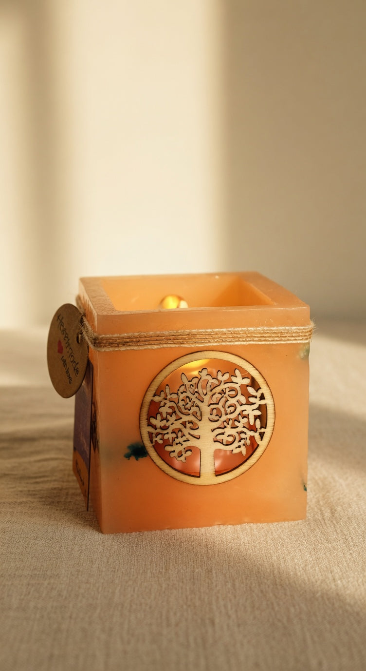 Vela hueca artesanal con símbolo del Árbol de la Vida en color naranja, iluminada con luz LED cálida. Pieza única hecha a mano con flores naturales.